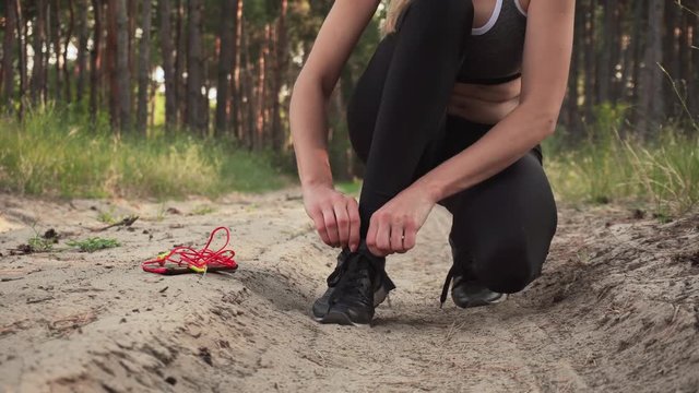 Athletic woman tying shoelaces on sports shoes and taking mobile phone with headphones