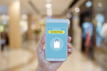 Hand holding smartphone with  text ONLINE MARKETING on screen over blurred in shopping mall background