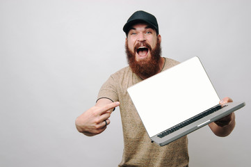 Excited young bearded man pointing at empty laptop screen