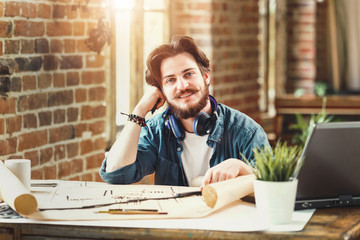 Male bearded architect smiling to the camera sitting at his desk at the office working on building plans copyspace creativity engineering project developing worker occupation career successful