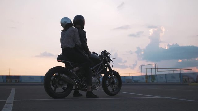 Young couple in helmets on motorcycle on the road with beautiful sunset sky background