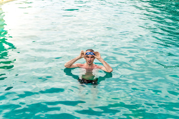 Sexy fit man with goggles relaxing in swimming pool