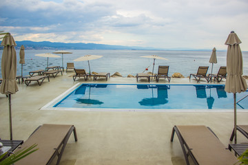 holidays rest concept of exterior empty patio with umbrellas and white furniture lounger near swimming pool and sea
