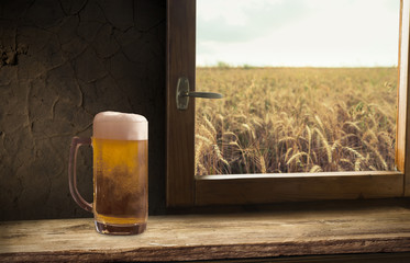 Glass of beer and bottle against wheat field and sunset