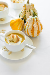 Two cups with fresh pumpkin cream soup decorated cream, seeds and crackers on white table cloth