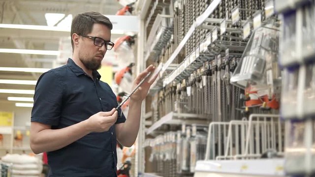 Customer man is choosing borers in a hypermarket. He is getting package from shelf and comparing different kinds, reading tags