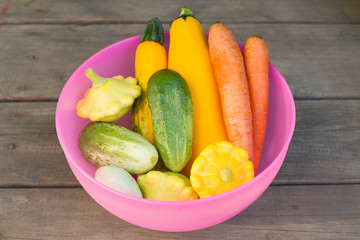Zucchini, squash, cucumber, tomato, carrots in a pink plate on a wooden table. Diet, a healthy lifestyle, healthy foods.