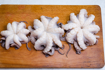 whole fresh raw octopus on cutting board closeup on rustic wooden table