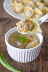Homemade meat and prawn wonton soup in white bowl on wooden table background.
