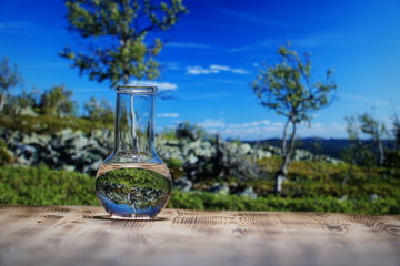 Clean water in a glass laboratory flask on wooden table on mountain background. Ecological concept, the test of purity and quality of water.
