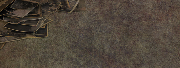 Rustic old photographs background banner- random pile of untidy sepia photographs in left corner with copy space on rustic grunge dark coloured background
