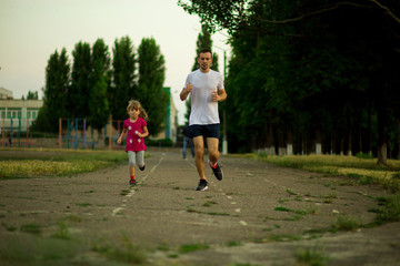 Athletic young father and little daughter running in stadium at sunset. Healthy lifestyle