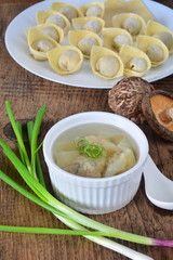 Homemade meat and prawn wonton soup in white bowl on wooden table background.
