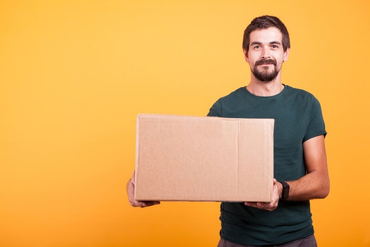 Attractive happy smiling delivery man with a cartboard box in his hands on yellow background in studio