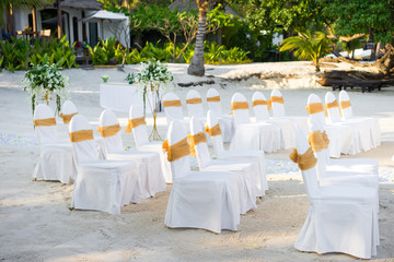 Beach wedding venue arrangement with spandex white cover chairs, gold organza sash on the white sand
