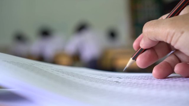 Education test concept : Hands student holding pen for testing exams writing answer sheet or exercise for taking fill in exam carbon paper computer on wood table at classroom in high school