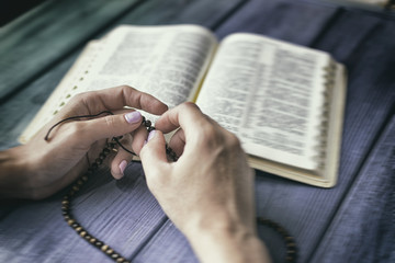 Appeal to God. Female hands with rosary on the Bible. Toned.