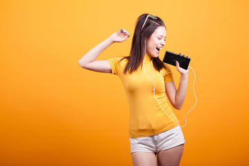 Cute young woman singing on her phone while dancing in studio on yellow background