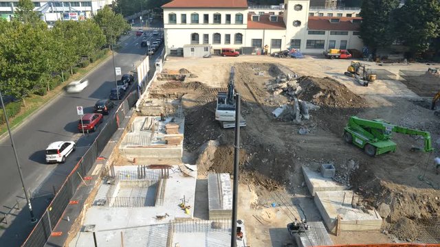 Aerial view of time lapse of a busy construction area, including laying foundations, manual workers, machinery, cranes and pouring cement - construction site concept