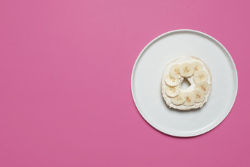 Banana and cream cheese bagel on a white plate on a pastel pink background