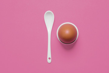 Soft boiled egg in eggcup with a white spoon on a pastel pink background