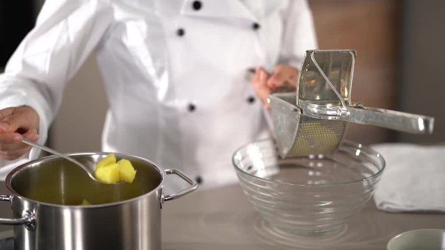 4K cooking footage, detail woman in cooks jacket taking cooked potatoes out of pot putting in potato ricer and pressing in to glass bowl kitchen
