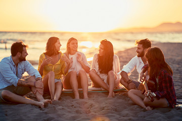 Friends with guitar at beach. friends relaxing on sand at beach with guitar and singing on summer sunset.