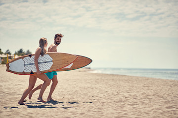 Happy couple surfers going together to surf at the beach .