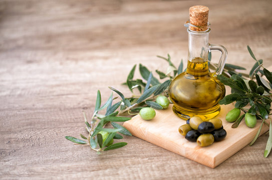green and black olives with olives branch and bottle of olive oil over wooden textured background.