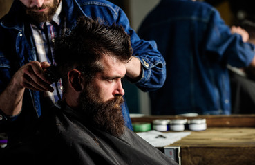 Hipster client getting haircut. Barber styling hair of bearded client with comb and clipper. Barber...
