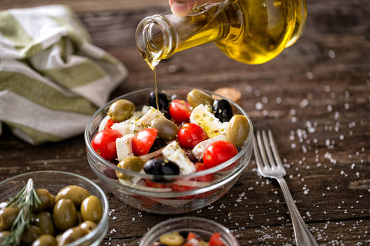 pouring virgin olive oil on vegetarian salad with fresh vegetables, feta and green olives.