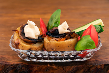 Potatoes stuffed with fried mushrooms with onions and carrots, baked in the oven, in a glass plate with sliced tomatoes, cucumbers and fresh Basil.