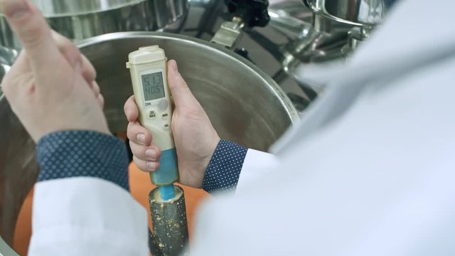 Close-up shot of hands of male technician testing beer with electronic device above brewing tun