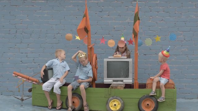 Happy brothers-boys in colored clothes and girl celebrate birthday of youngest boy on pirate ship. Girl and boy are dressed in carnival hat for parties. Children are happy together. 3 years
