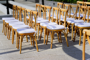 Wooden folding lawn chairs line up in a row with white seat for outdoors wedding venue settings