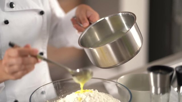 4K cooking footage, close up female cook putting melted butter out of pot over farina, eggs and potatoes in glass bowl for fresh selfmade dough in kitchen

