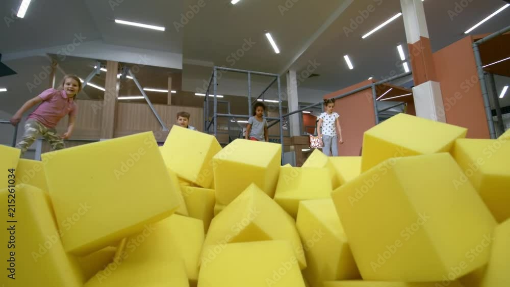 Wall mural front view of four multi ethnic children jumping towards camera into cube pit with yellow soft foam 
