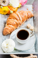Fresh Croissant, Cup of Coffee and Ranunculus Flowers. Breakfast