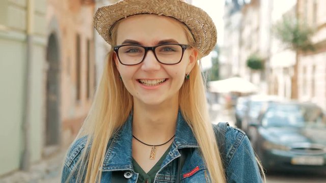 portrait of a happy beautiful blond girl with glasses, a hat and a blue jeans jacket.