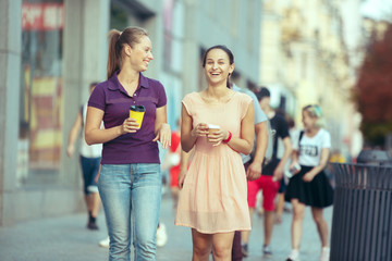 Obraz premium Beautiful girls holding paper coffee cup and enjoying the walk in the city
