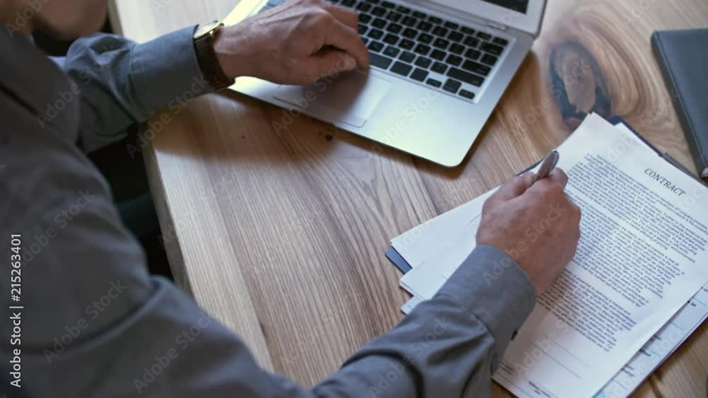 Poster hands of unrecognizable middle-aged businessman taking notes in text of contract when working on lap