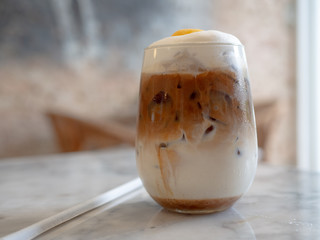 A cup of ice cappuccino with latte art and organic coffee beans on table.