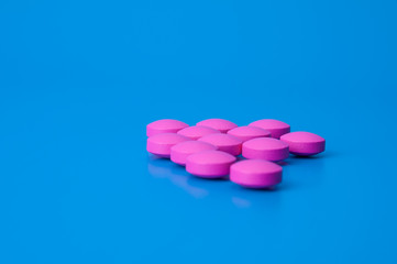 Obraz na płótnie Canvas Bright pink pills on a blue background. Location in the middle of the image