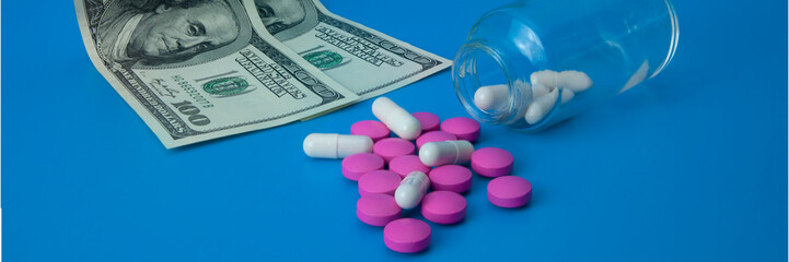 On a blue background, pills scattered from a jar and two bills of one hundred dollars.