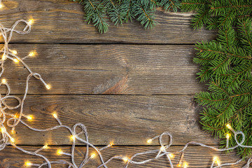 Christmas close-up of Christmas tree branches and Chistmas lights on vintage wooden background. Top view of a Christmas workplace. New Year frame or Xmas Mockup.