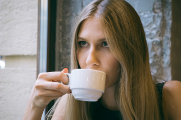 Young beautiful girl eats and drinks in a coffee shop. Close-up on the face model. Cup of coffee or tea with sweet delicious cake. Concept of a date or meeting with a person. Trendy look