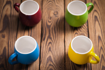 Four colored empty ceramic clean mugs on old worn brown wooden table