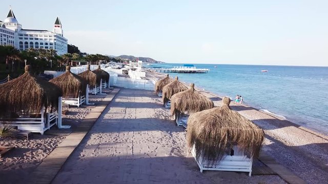 Aerial view of the waves, sandy beach with reed umbrellas. Video. Top view of the sandy beach with natural umbrelas