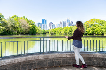 One young woman standing in Piedmont Park in Atlanta, Georgia looking at scenic view, water, cityscape, skyline of urban city skyscrapers downtown, Lake Clara Meer