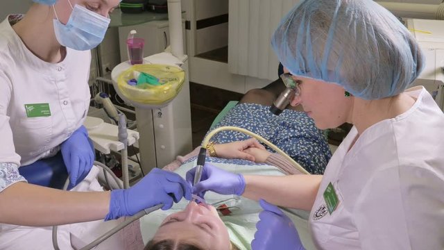 Woman at dentist clinic gets dental treatment to fill a cavity in a tooth. Dental restoration and composite material polymerization with UV light and laser. The doctor works with an assistant.